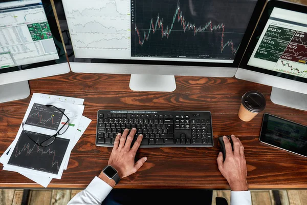 Achieve best. Top view of businessman, trader working, sitting by desk in front of multiple computer monitors. Stock trading forex with technical indicator tool. Hands on keyboard.