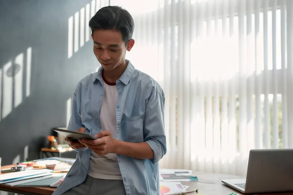 Δημιουργική δουλειά. Πορτρέτο του νεαρού Ασιάτη χρησιμοποιώντας touchpad ενώ ακουμπά σε ένα τραπέζι στο σύγχρονο γραφείο. Εστιασμένη σχεδιαστής σε casual ρούχα που εργάζονται με ψηφιακή ταμπλέτα — Φωτογραφία Αρχείου