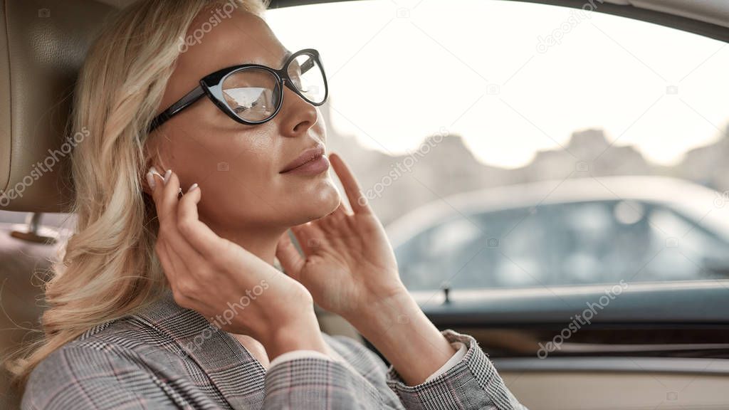 Music is my inspiration. Attractive and stylish businesswoman keeping eyes closed and listening music while sitting on drivers seat in the car