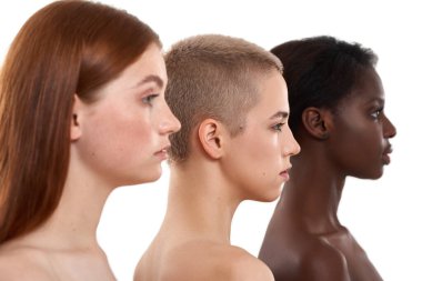 Farklı ten renkleri. Üç güzel, çok kültürlü genç kadının yan görüntüsü. İki beyaz arka plan üzerinden stüdyoda poz veren beyaz ve Afrikalı yarı çıplak kadın. Doğal güzellik.