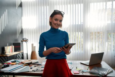 İşimi çok seviyorum. Gündelik giysiler içindeki mutlu genç bayan tasarımcının portresi dokunmatik ped tutuyor ve modern ofiste dururken kameraya gülümsüyor. Dijital tabletle çalışan grafik tasarımcısı