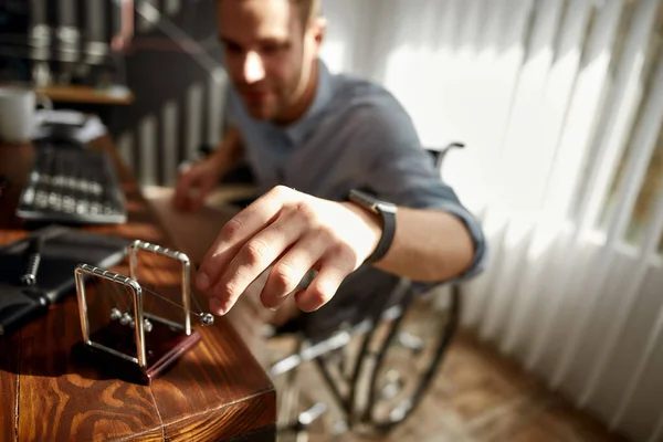 Beskuren suddig bild av en affärsman i rullstol flytta Newton bollar medan sitter på sin arbetsplats på kontoret. Arbetstagare med funktionshinder — Stockfoto