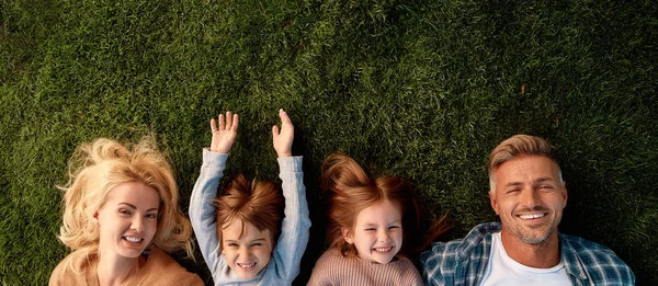 Mantén la calma y ama a tu familia. Familia feliz de cuatro tumbados sobre hierba verde —  Fotos de Stock