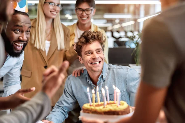 最美好的祝愿年轻快乐的男人一边在蛋糕上吹蜡烛，一边在笑容满面的混血儿商人中庆祝生日 — 图库照片