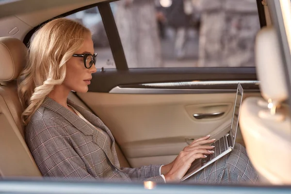 Kluczem do sukcesu w biznesie. Widok z boku pięknej i pewnej siebie kobiety w pełnym garniturze pracującej na laptopie siedząc w samochodzie — Zdjęcie stockowe
