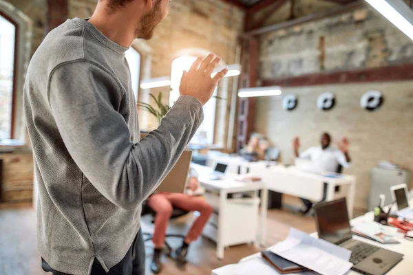 If you dont like something change it. Young man in casual wear holding box with personal things and saying good bye to his ex-colleagues while leaving modern office