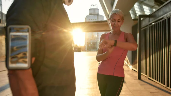 Grandes resultados. Mujer hermosa y en forma de mediana edad en ropa deportiva mirando smartwatch mientras entrena con su marido al aire libre — Foto de Stock