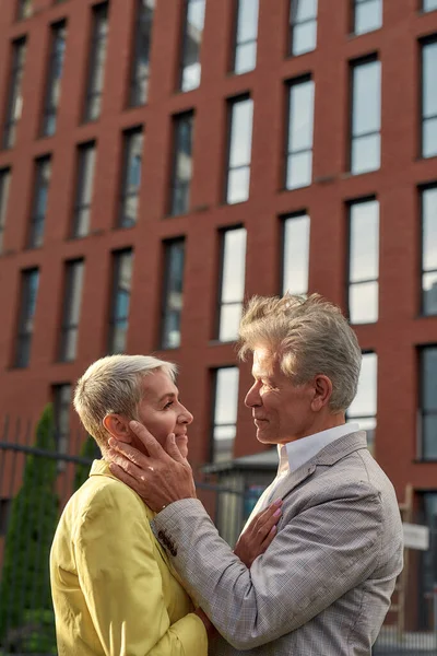 You are the love of my life. Handsome middle-aged man in touching face of his beautiful wife and looking in her eyes while standing together outdoors