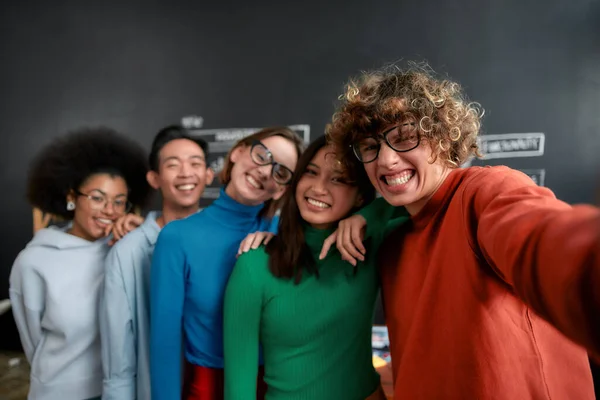 Mi godo il tempo insieme. Positivo gruppo di persone multiculturali in abbigliamento casual fare selfie al telefono mentre in piedi contro lavagna in ufficio creativo — Foto Stock