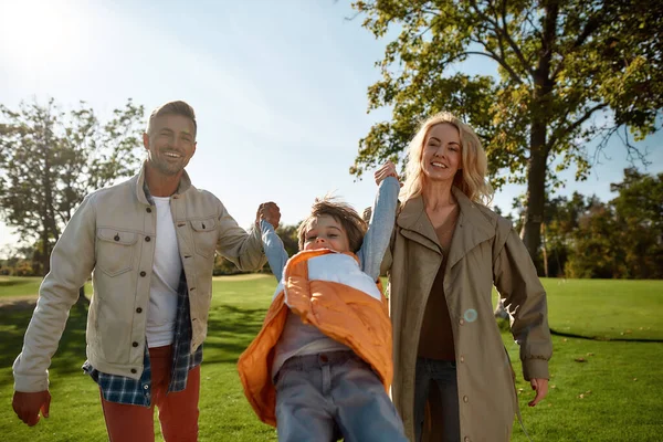 En el momento de la prueba, la familia es la mejor. Padres felices levantando niño juguetonamente — Foto de Stock