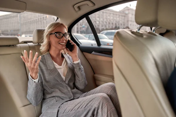 Udało nam się. Podekscytowana bizneswoman w klasycznym stroju siedzi w samochodzie i rozmawia przez telefon ze swoim partnerem biznesowym — Zdjęcie stockowe