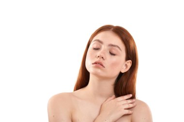 Just dreaming. Young sensual red-haired girl with freckles on face keeping eyes closed and thinking about something while standing against white background. Natural beauty