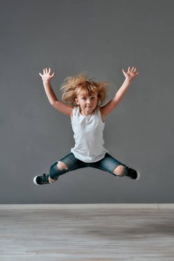 Crazy child. Full length portrait of a cute and excited little girl in casual clothes jumping in studio and looking at camera