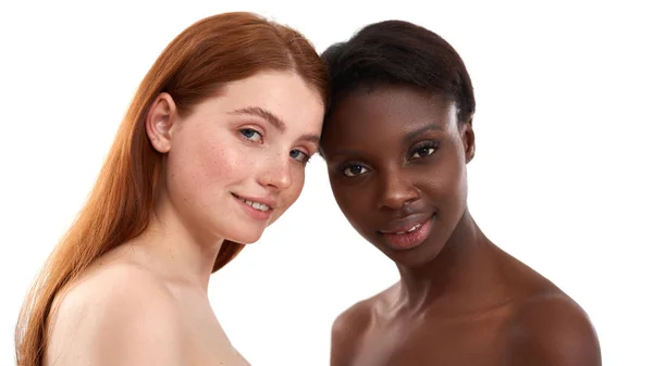 Milk and chocolate. Two multicultural young women with soft glowing skin looking at camera and smiling while posing in studio over white background. African and caucasian women standing together — 图库照片