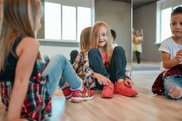 Taking a break. Portrait of cute and fashionable little girl leaning on the mirror and looking at camera with smile while sitting on the floor with kids in the dance studio — Stockfoto