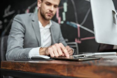 Bugün akıllıca bir hareket yap. Ofiste çalışırken bilgisayar monitörünün önünde oturan genç bir tüccar. Arkaplanda dosya ve veri analizleriyle dolu bir karatahta.