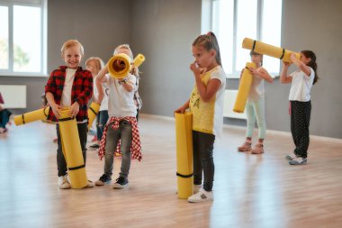 Jimnastik egzersizleri. Ellerinde yoga minderleri olan ve dans stüdyosunda durup eğlenen bir grup hoş çocuk.
