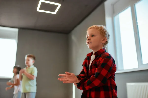 Coole Tänzerin. Porträt eines kleinen süßen Jungen im karierten roten Hemd, der während eines Choreografiekurses tanzt. Kindergruppe lernt in der Tanzschule — Stockfoto