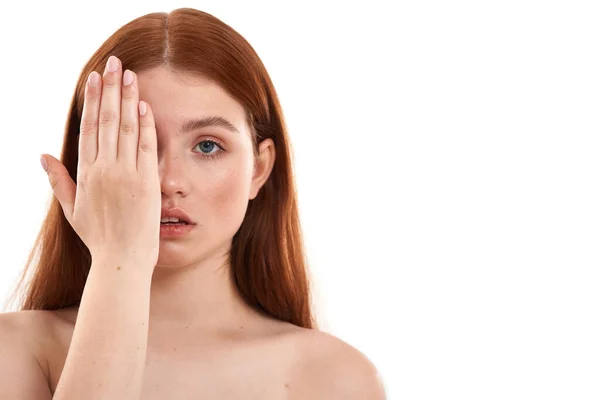 Uma mulher perfeita. Retrato de uma jovem sensual menina ruiva com sardas no rosto cobrindo metade do rosto com a mão e olhando para a câmera enquanto está de pé contra o fundo branco — Fotografia de Stock