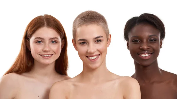 Belleza natural. Tres alegres mujeres jóvenes multiculturales mirando a la cámara y sonriendo mientras están de pie sobre un fondo blanco. Hermosas modelos con pelo negro, rojo y rubio de pie en fila —  Fotos de Stock