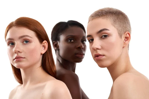 Retrato de tres hermosas mujeres jóvenes multiculturales con hombros desnudos posando en estudio sobre fondo blanco. Hermosas modelos con pelo negro, rojo y rubio de pie juntos — Foto de Stock