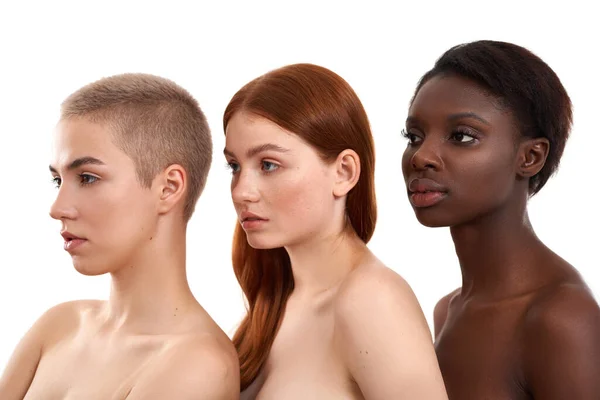Beleza na Diferença. Vista lateral de três belas multiculturais jovens mulheres de pé perto umas das outras em estúdio contra fundo branco — Fotografia de Stock