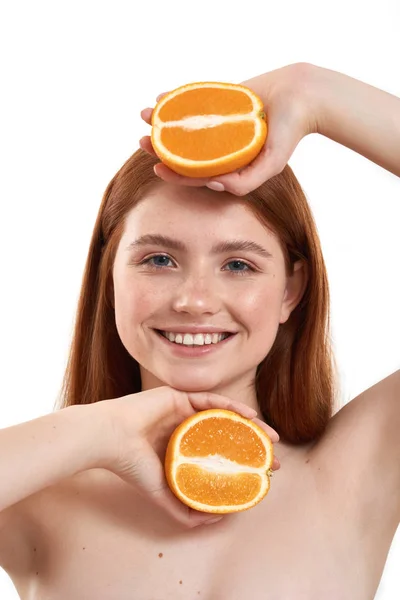 护肤水果。年轻而快乐的红头发女孩的画像，脸上有雀斑，手里拿着两片橙子，站在白色背景下对着相机微笑 — 图库照片