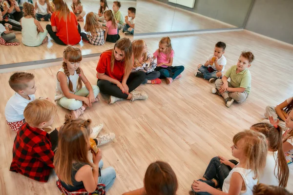 Sto analizzando gli errori. Un gruppo di piccole ballerine sedute sul pavimento si è riunito intorno alla loro insegnante di danza femminile e l'ha ascoltata attentamente. Scuola di danza — Foto Stock