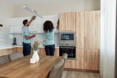 Temizle şunu. Modern mutfak mobilyalarını mikro fiber bezle temizleyen üniformalı iki genç profesyonel temizlikçinin arka görüntüsü. Profesyonel temizlik ekibi çalışıyor.