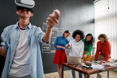 Dünyayı değiştiren teknolojiler. Sanal gerçeklik kulaklığı takıp gülümseyen Asyalı genç bir adam meslektaşları arkasında yeni bir projeyi tartışırken. Yüksek Teknoloji