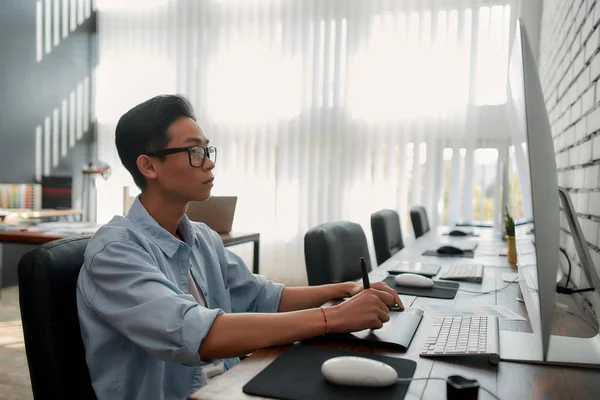 Creating Beauty. Side view of a young asian graphic designer is using digital graphics tablet while sitting at his workplace in the creative agency. Design Studio — Stock Photo, Image