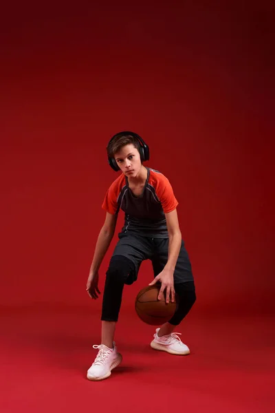 Bawa ke Net. Seorang remaja laki-laki terlibat dalam olahraga, melihat kamera sambil berolahraga dengan bola basket. Terisolasi di latar belakang merah. Fitness, pelatihan, konsep gaya hidup aktif. Tembakkan vertikal . — Stok Foto