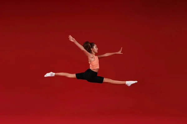 Будь лучшим. Симпатичный малыш, девочка занимается спортом, она в движении, прыгает в воздухе. Изолированный на красном фоне. Фитнес, тренировки, концепция активного образа жизни. Горизонтальный выстрел — стоковое фото