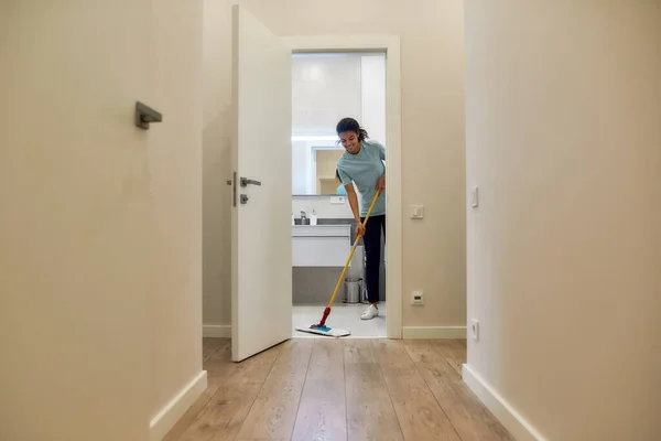 Einfache Reinigung. Junge Afroamerikanerin putzt Boden mit Wischmopp und lächelt — Stockfoto