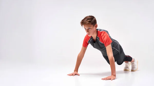 让你自己更坚强拍摄了一个十几岁男孩参加体育活动的全景照片，在做俯卧撑的时候看起来很专注。被白色背景隔离。培训、积极生活方式概念 — 图库照片