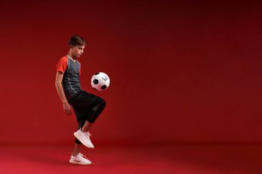 Nasıl gol atılacağını biliyorum. Genç bir çocuk sporla meşgul, onunla antrenman yaparken futbola bakıyor. Kırmızı arka planda izole edilmiş. Fitness, eğitim, aktif yaşam tarzı konsepti. Yatay çekim.