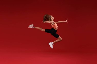 Elinizden geleni yapın. Şirin bir çocuk, kız sporla meşgul, havada zıplıyor. Kırmızı arka planda izole edilmiş. Fitness, eğitim, aktif yaşam tarzı konsepti. Yatay çekim