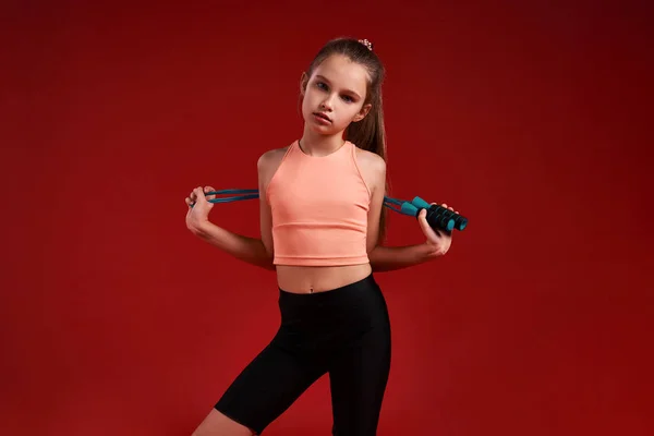 Επαγγελματίας. Ένα χαριτωμένο κορίτσι ασχολείται με τον αθλητισμό, που κοιτάζει κάμερα, ενώ στέκεται με σχοινάκι άλμα. Απομονωμένο σε κόκκινο φόντο. Γυμναστική, εκπαίδευση, ενεργός τρόπος ζωής. Οριζόντια βολή — Φωτογραφία Αρχείου