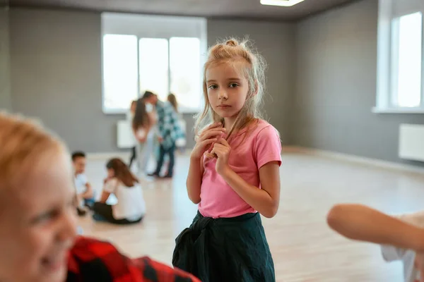 Dance school. Portrait of a little cute girl looking at camera while standing in the dance studio. Group of children having a choreography class — 스톡 사진