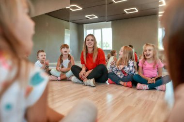 Spending time with kids. Portrait of positive female dance teacher with group of happy children sitting on the floor in the dance studio
