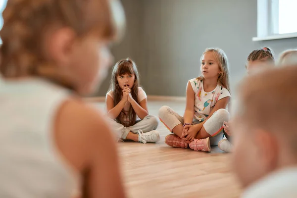 Having a break. A group of little cute girls sitting on the floor in the dance school. Choreography class. Little dancers sitting on the floor gathered around their female teacher — 스톡 사진
