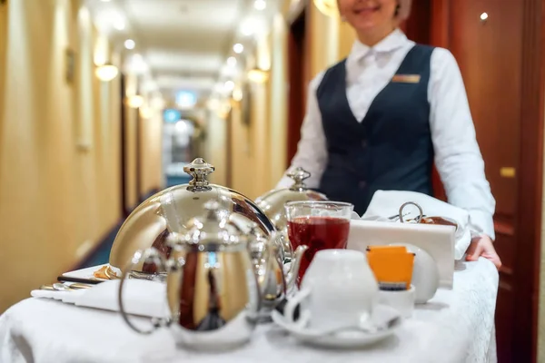 Tudo o que precisas. Garçonete de uniforme entregando bandeja com comida em um quarto de hotel. Serviço de quartos. Concentre-se em utensílios de mesa — Fotografia de Stock