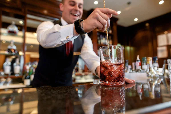 Mestre do Cocktail. Tiro cortado de jovem barman de pé no balcão e misturando ingredientes enquanto faz coquetel gelado no bar — Fotografia de Stock