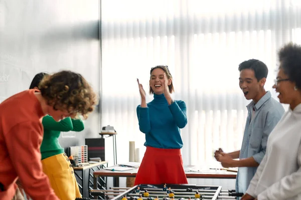 Noi siamo i vincitori. Giovani e felici multiculturali in abbigliamento casual che giocano a calcio balilla nell'ufficio moderno. Attività d'ufficio. Ci divertiamo insieme. Lavoratori felici — Foto Stock