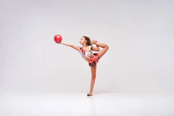 Немає гравітації. Повнометражний знімок гнучкої милої дівчинки-гімнастки, яка виконує акробатичні вправи, використовуючи м'яч ізольовано на білому тлі. Спорт, навчання, ритмічна гімнастика, концепція активного способу життя — стокове фото