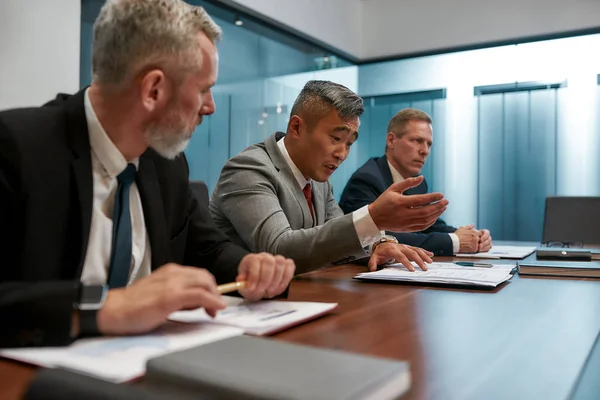 Discutere i dettagli del contratto. Business team multiculturale in abiti formali che lavorano insieme mentre sono seduti alla scrivania dell'ufficio. Discutere i dettagli del progetto alla riunione — Foto Stock