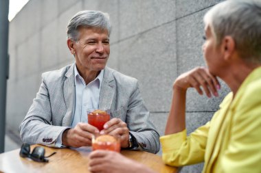 Seni gördüğüme sevindim. Resmi giyinmiş yakışıklı bir adam elinde kokteyl tutarken ve kafede birlikte otururken gülümseyerek kız arkadaşına bakarken.