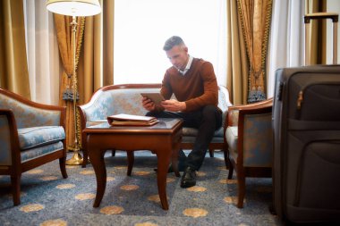 Konsantrasyon rahat bir yerde. Girişten sonra otel odasındaki kanepede otururken iş adamının tablet bilgisayar kullanırken tam boy görüntüsü. İş gezisi konsepti.