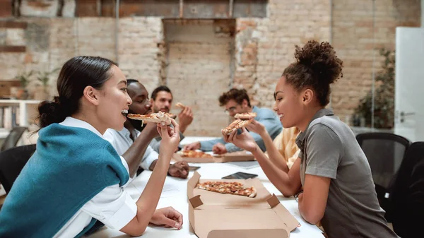 Time for a lunch. Happy multicultural team eating pizza and communicating with each other while sitting together in the modern office — Φωτογραφία Αρχείου