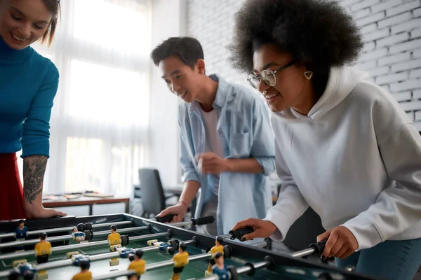 Super divertido. Grupo de jóvenes y felices multiculturales en ropa casual jugando futbolín en la oficina creativa. Actividades de oficina. Divirtiéndose juntos. Empleados felices —  Fotos de Stock